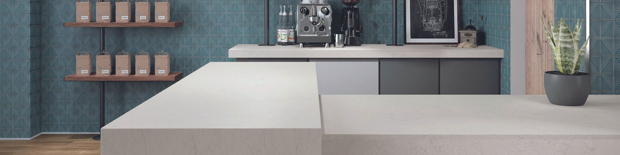 Coffee shop with off-white stone look quartz countertops, textured blue diamond-shaped wall tile, floating shelves holding cups and bags of coffee.