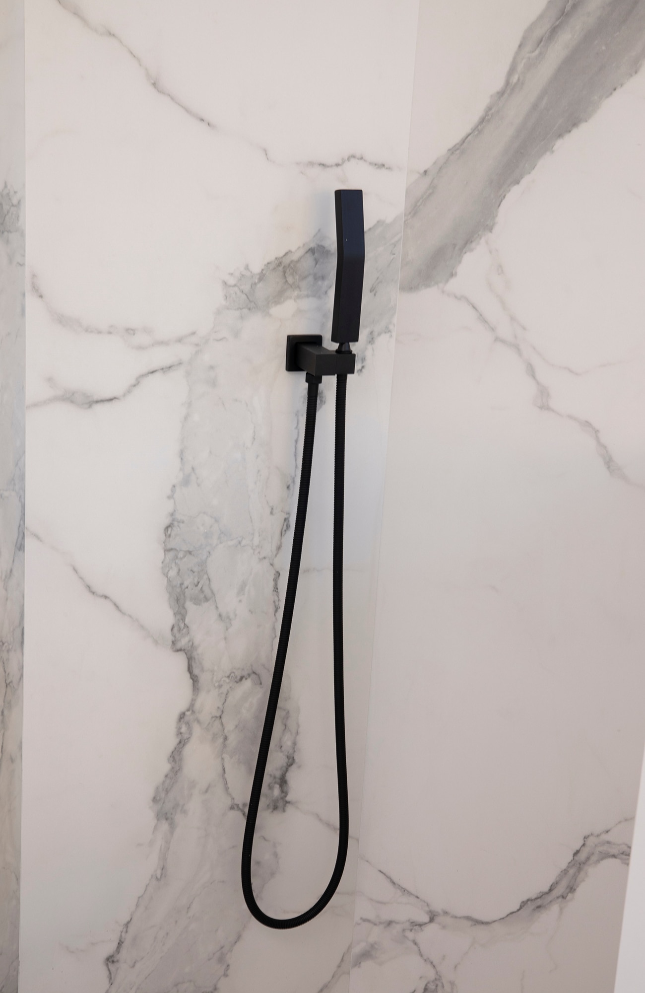 Closeup of a steam room wall with black fixtures and white with gray veining porcelain slab that looks like marble.