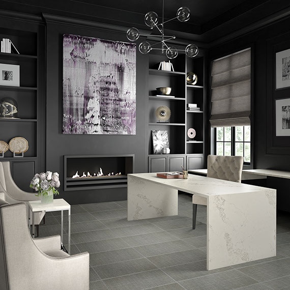 Home office with gray floor tile that looks like linen fabric, desk made of white quart with gray veining, wall-mounted fireplace, dark gray built-in and walls.