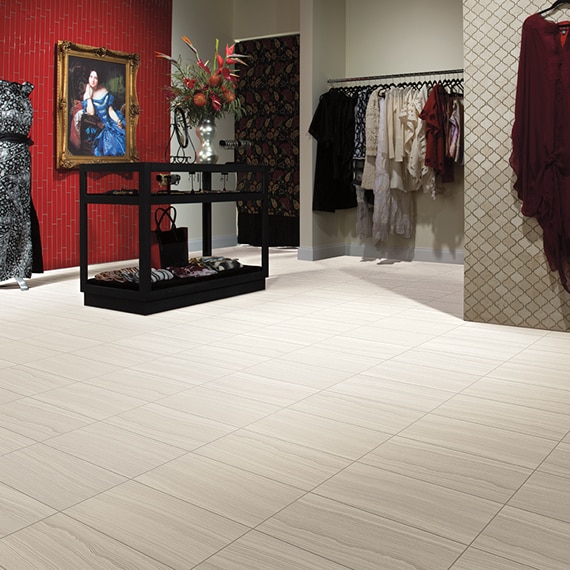 Dress shop with beige tiles for flooring that look like fabric, feature wall with red glass tile, mannequin wearing long gray dress, and tan arabesque wall tile. 