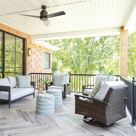 Renovated patio with floor tile that looks like wood plank flooring installed in a herringbone pattern, wicker sofa and chairs with white cushions.