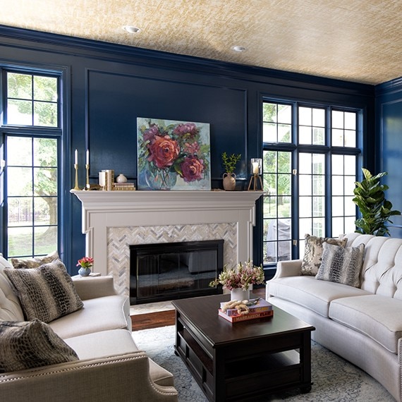 Renovated living room with dark blue paneled walls, fireplace with gray & beige marble mosaic surround and hearth, and white mantel.