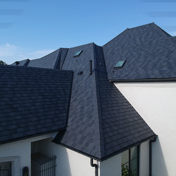 Bird's eye view of black slate-looking porcelain roofing tiles on white brick home.