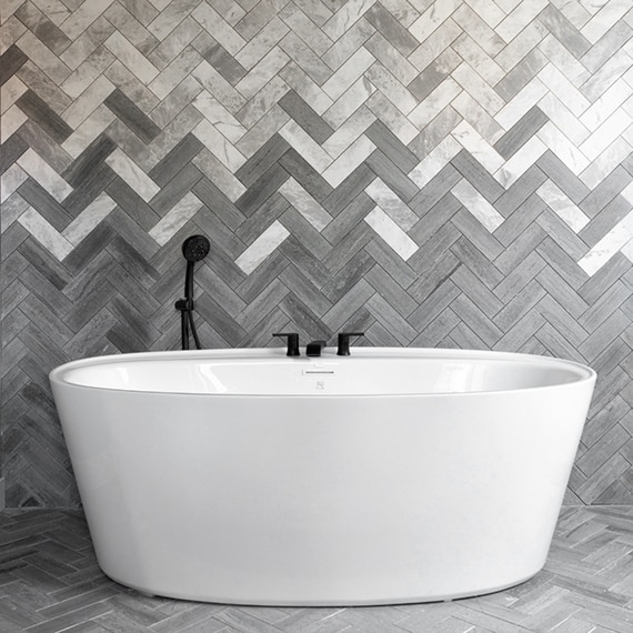 Freestanding soaking bathtub in front of chevron backsplash of white & gray marble tile blended with gray limestone tile.