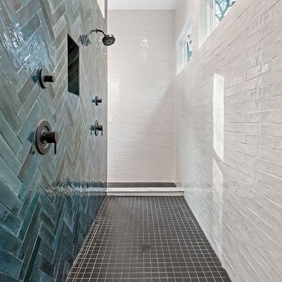 Renovated shower with glossy white subway wall tile, glossy teal herringbone wall tile, black fixtures, and black mosaic shower floor tile.