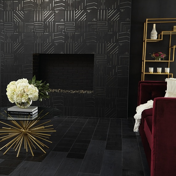 Living room fireplace with black geometric tile, crimson velvet chairs, coffee table with bouquet of white hydrangeas, and black wood look tile.