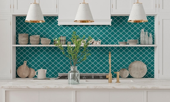 Bold kitchen décor with cream marble island countertop, bright teal arabesque mosaic tile backsplash, white cabinets, and floating shelves.