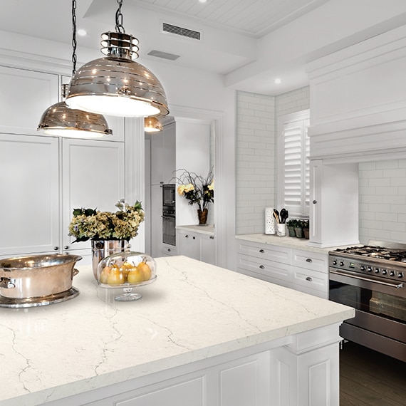 Fresh and clean kitchen décor with white subway tile backsplash, white quartz countertop & island, stainless steel gas stove, and white cabinets.