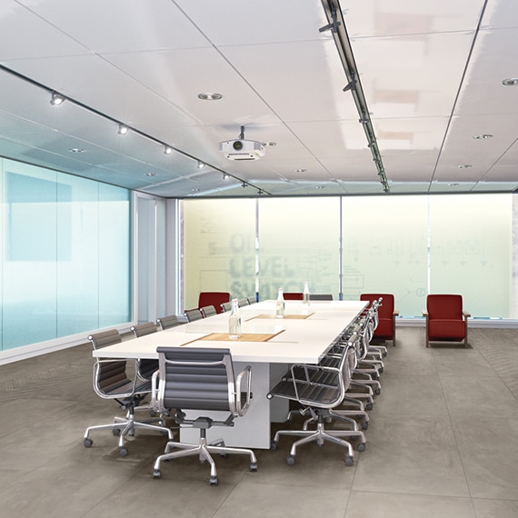 Conference room with gray tile flooring that looks like concrete, frosted glass walls, long white table with gray & silver rolling chairs, and red side chairs.