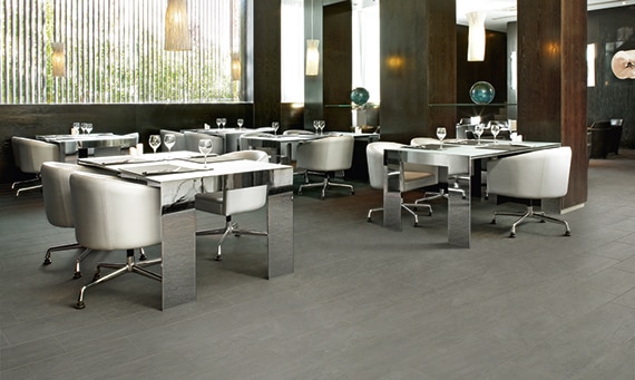 Restaurant with gray floor tile that looks like concrete, mirrored tables with white leather rolling chairs, wood pillars, and large picture window.