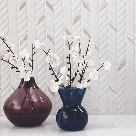 Closeup of textured wall with white leaf-shaped mosaic tile, blue and maroon vases holding white flowers.