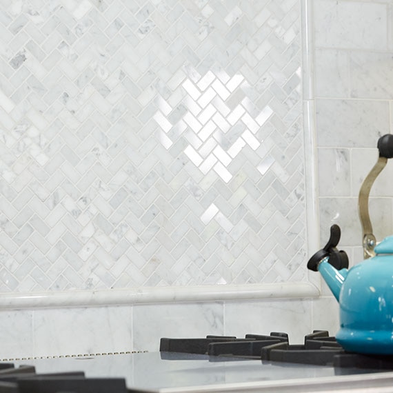 Closeup of white marble backsplash behind the stovetop with raised pencil trim outline and teal teapot on the stove.