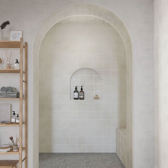 Shower with intentionally imperfect gray wall tile, arched opening, bench and niche, gray penny round mosaic shower floor tile with antimicrobial properties.