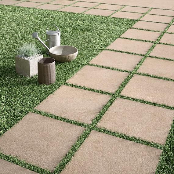 Outdoor walkway made of 2 cm porcelain gray stone look pavers laid on thick green grass.