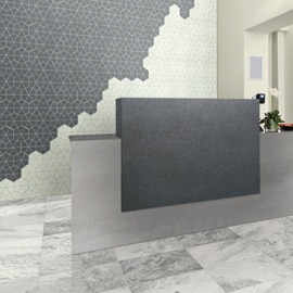 Reception area with gray marble floor tile, desk of silver metallic look & charcoal stone look porcelain slab, and gray & cream kaleidoscope mosaic wall tile.