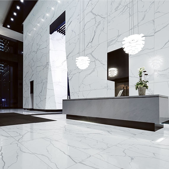 Commercial reception area with tall ceilings. Walls and floor are covered in extra large-format porcelain slab in a classic white marble look.