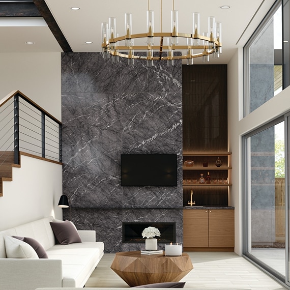 Living room with porcelain slab fireplace that looks like black marble with white veins, wood dry bar, white sofa, and floor-to-ceiling windows. 