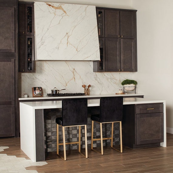 Kitchen with white & beige marble-look porcelain slab backsplash & vent hood, white quartz countertop on island, wood-look floor tile.