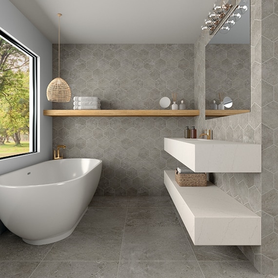 Scandinavian style bathroom with gray floor tile and gray hexagon wall tile that looks like stone, soaker bathtub, and floating white quartz vanity.