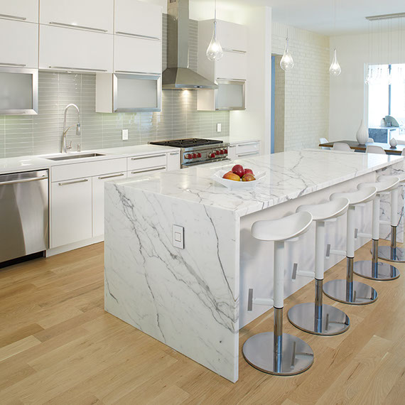 Elegant kitchen with white & gray vein marble waterfall island, white quartz countertop, gray glass mosaic backsplash, and white cabinets.