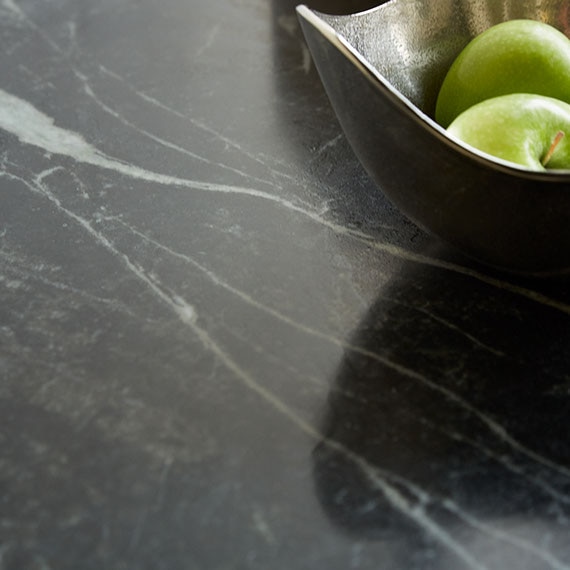 Close up of grey-veined green soapstone countertop with silver bowl of green apples.