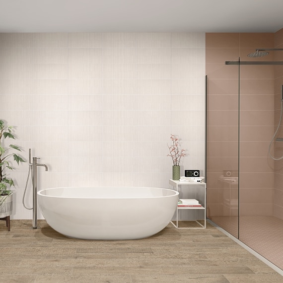 Bathroom with tan stone look floor tile, soaker tub in front of wall of white textured tile, separate shower with mauve tile and frameless glass doors.