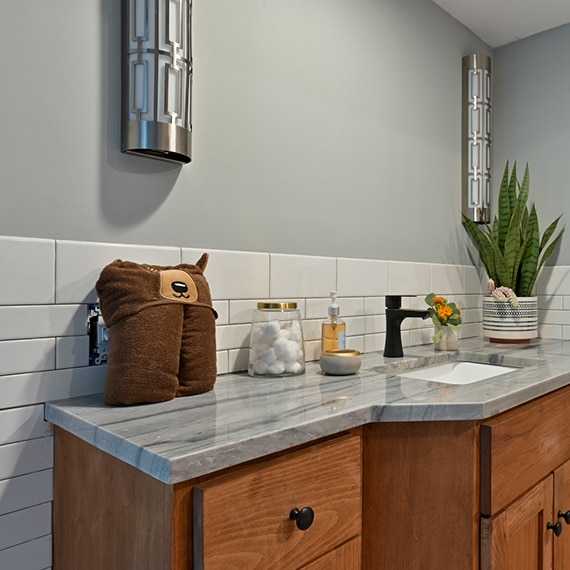 Children’s bathroom with gray quartzite countertop with heavy striations on a vanity of natural wood cabinets, and white ceramic tile backsplash/wainscot.