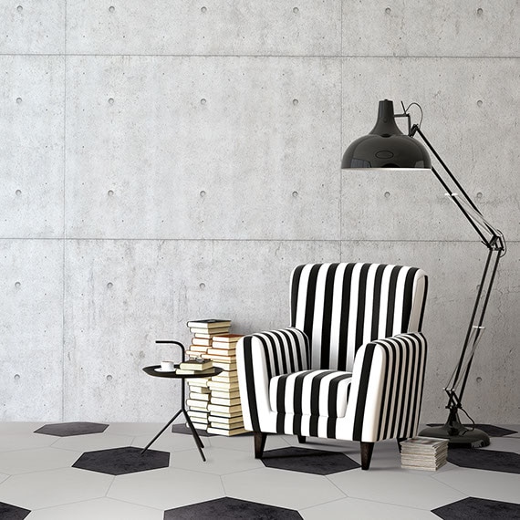 Sitting area with raw cement walls and black and white twenty-inch hexagon floors. Black and white striped armchair and black floor lamp in the background.