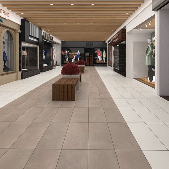 Shopping mall with brown and beige concrete look floor tile, wood benches around concrete planters, store windows with mannequins in women’s clothing, and ceiling wood beams.