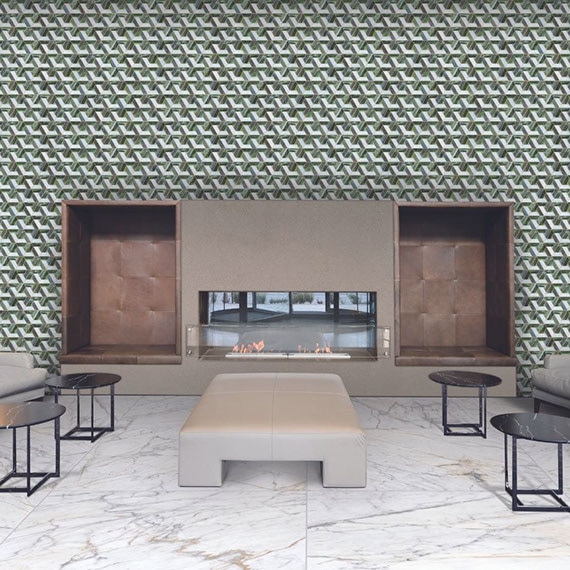 Hotel lounge area with green and white glass mosaic tile feature wall with electric fireplace, white & gray marble-look floor tile, and leather chairs & ottoman.
