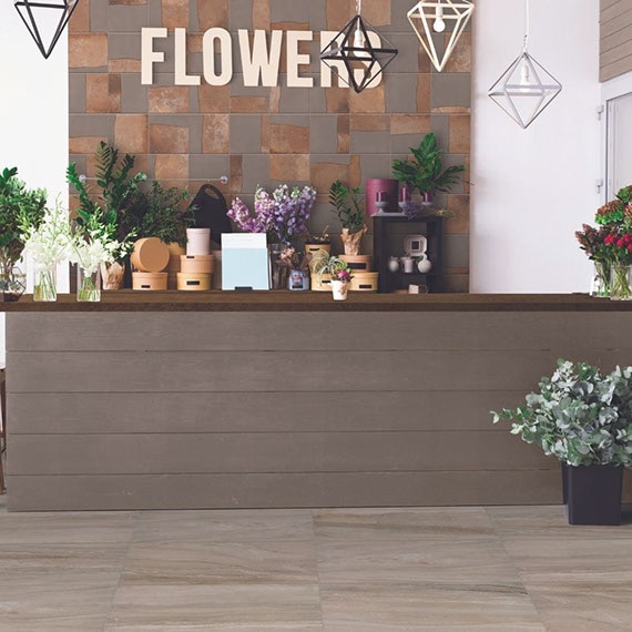 Flower shop with floor tile that looks like brown marble, feature wall with brown tile with copper-colored accents, and reception counter with vases of flower and greenery bouquets.
